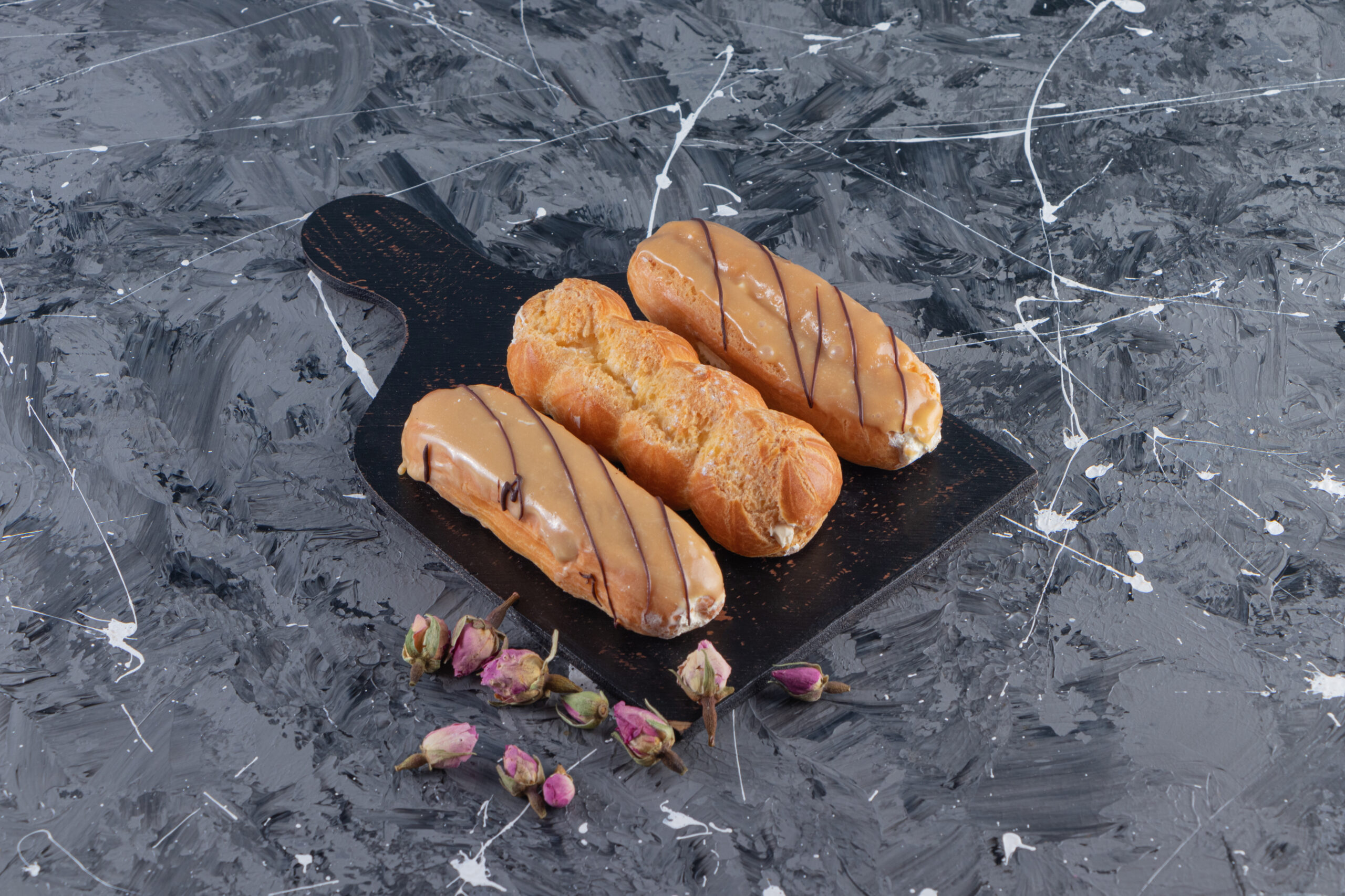 black cutting board of delicious eclairs on marble background